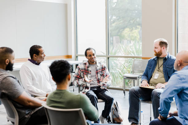 Diverse men listen to young man sharing in therapy meeting