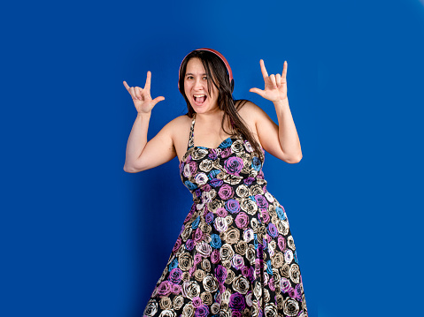 A middle aged, mixed race, woman poses at the studio. She is happy and full of joy wearing a fun dress.