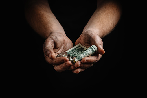 The dirty hands of a homeless man, a poor man holding not much money, dollars. The concept of helping homeless and underprivileged people. Conceptual image of dirty hands holding a few dollars. Financial crisis. Collapse in the economy