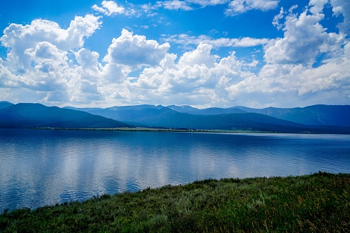 A beautiful shot of a lake surrounded by mountains against a blue cloudy sky on a sunny day
