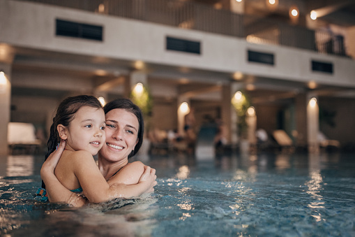 Two people, young mother in hotel swimming pool with their little daughter.