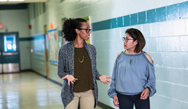 istock Multiracial teachers converse, walking in school hallway 1454256640