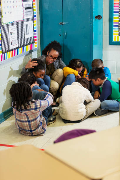 l’enseignant et les enfants font un exercice de sécurité à l’école, le confinement - arm around caucasian latin american and hispanic ethnicity child photos et images de collection