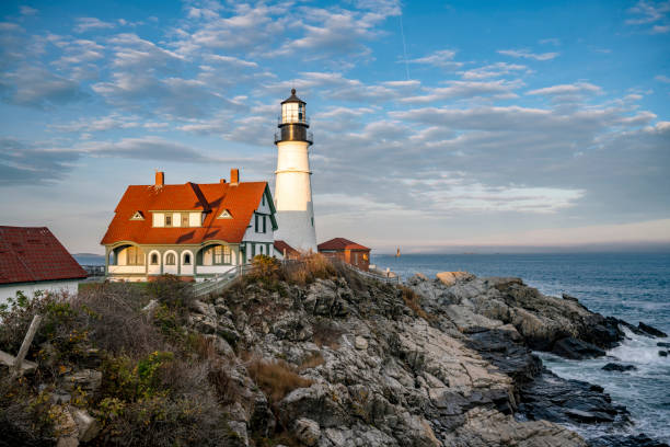 An active lighthouse on a rocky shore of the Atlantic Ocean in the rays of the setting sun in the state of Maine in New England stock photo