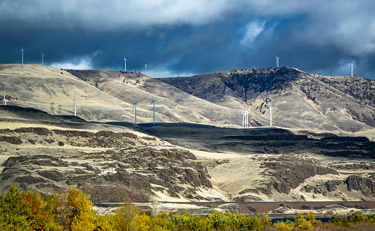 Landscaping with electric wind generators cluster to transform wind energy into electrical energy on top of a bare hills ridge with cloudy sky along the Columbia River in Washington State