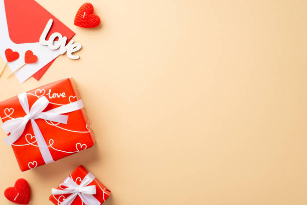 istock Valentine's Day concept. Top view photo of red present boxes with bows envelope with letter paper hearts candles and inscription love on isolated pastel beige background with blank space 1454260235