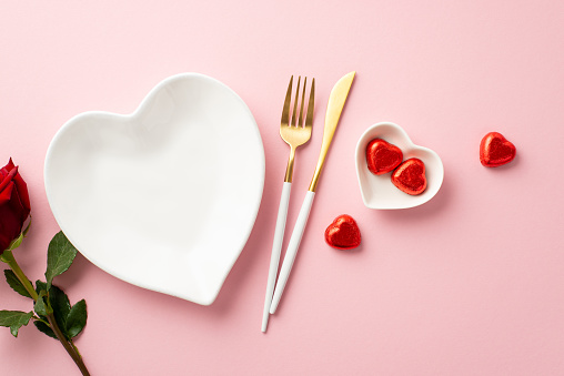 Valentine's Day concept. Top view photo of heart shaped dish cutlery chocolate candies and rose on isolated pastel pink background with copyspace