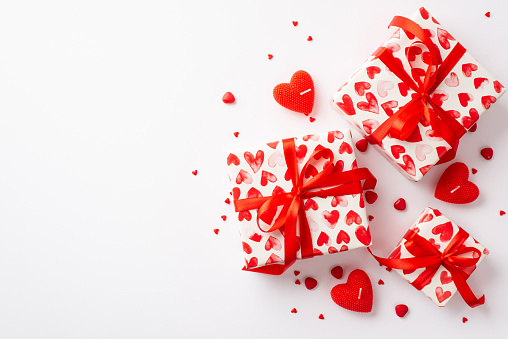 St Valentine's Day concept. Top view photo of gift boxes in wrapping paper with heart pattern candles and sprinkles on isolated white background with blank space