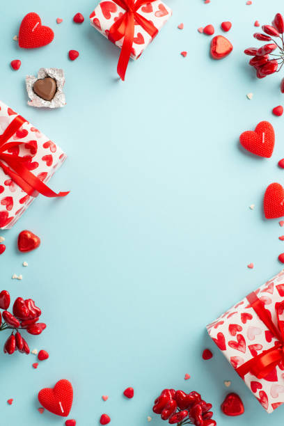 valentine's day concept. top view vertical photo of gift boxes with ribbon bows heart shaped chocolate candies candles and sprinkles on isolated pastel blue background with copyspace in the middle - valentines day candy chocolate candy heart shape imagens e fotografias de stock