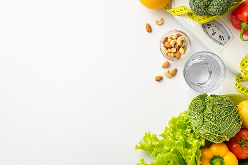 Slimming concept. Top view photo of tape measure glass of water vegetables cabbage cauliflower lettuce tomato pepper almond cashew nuts and scales on isolated white background with copyspace