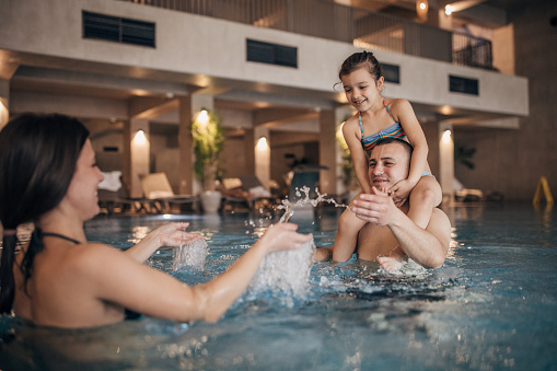 Group of people, husband and wife together in hotel swimming pool with their little daughter having fun.