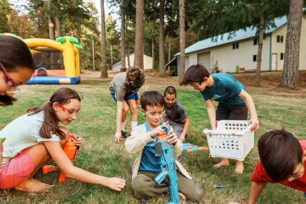 A multiracial group of elementary age and tween boys and girls prepare to play with nerf guns in the back yard during a birthday party.