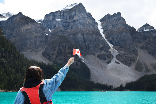 Young girl in life vest in canoe on turquoise blue Moraine lake holding high small canadian flag