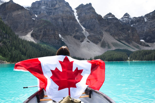 Young girl in a canoe holding canadian flag with spread out arms Young girl in a canoe from behind holding canadian flag spreading her arms, surrounded by turqouise blue lake Moraine and mountains canada stock pictures, royalty-free photos & images