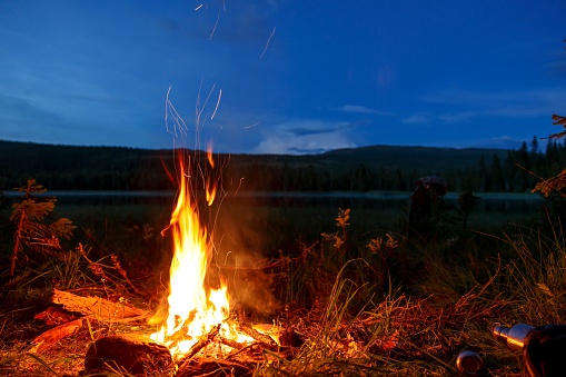 A closeup of a lit campfire by a lake in the Nordic mountains at night