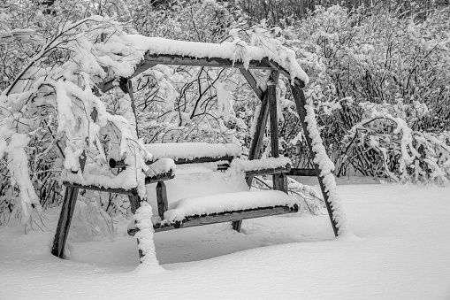 A bench style garden bench covered with freshly fallen snow after a snowstorm.