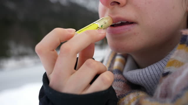 CLOSE UP of young woman applying lip balm, she smiles