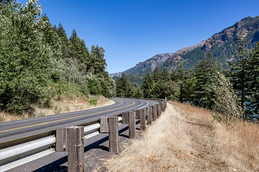 Scenic summer landscape with a winding mountain highway road with security fence and trees in Columbia Gorge area allows tourists and travelers to visit all corners of the famous national reserve