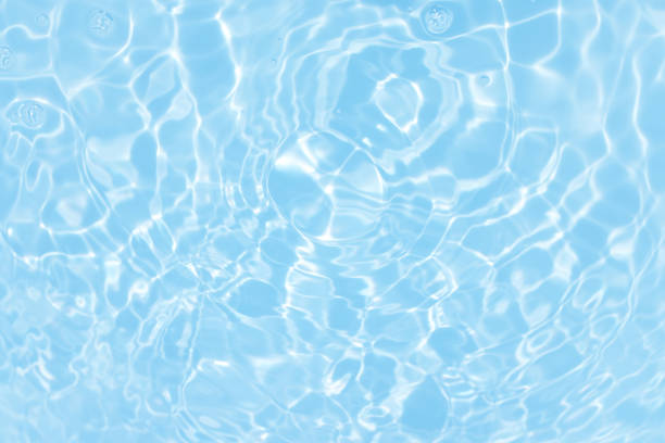 Defocus blurred transparent blue colored clear calm water surface texture with splashes and bubbles. Trendy abstract nature background. Water waves in sunlight with caustics. Blue water spay shinning