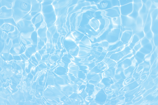 Defocus blurred transparent blue colored clear calm water surface texture with splashes and bubbles. Trendy abstract nature background. Water waves in sunlight with caustics. Blue water spay shinning