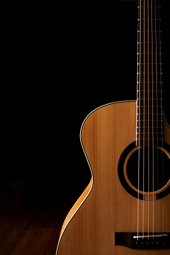 Classic Acoustic guitar close up, dramatically lit on a black background with copy space