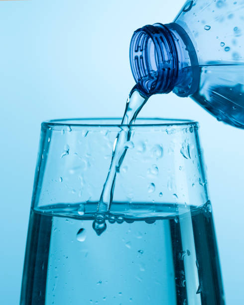 istock Water pouring from a plastic bottle into a glass beaker on a blue background 1454305802