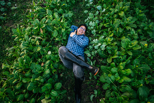 Portrait of Happy Asian farmer man rested comfortably in the middle of the field after finishing his work. Agricultural business, relexing and lifestyle concepts.