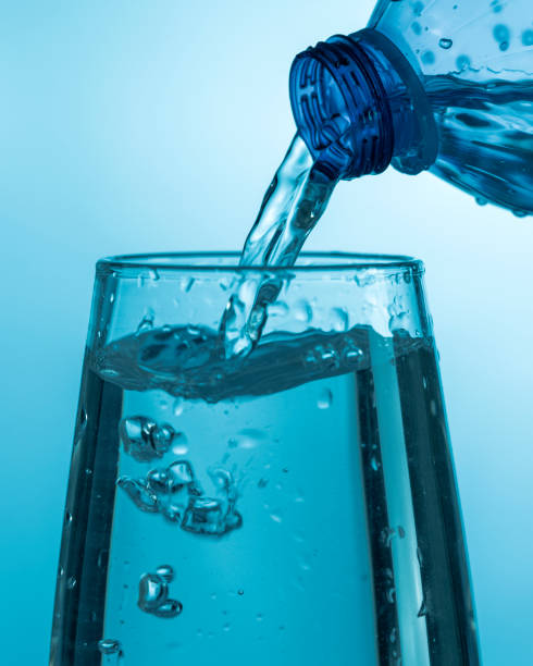 istock Water pouring from a plastic bottle into a glass beaker on a blue background 1454305820