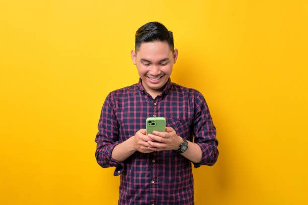 istock Smiling young Asian man using smartphone for messaging with friends isolated over yellow background 1454306215