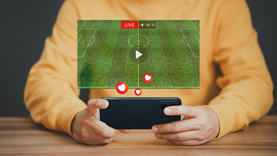 Man using a smartphone or mobile phone for watching live football streaming online on virtual screen, searching video on internet, concept of content online.