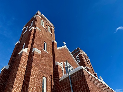 Church and blue sky view in Vulcan, Michigan in The Upper Peninsula of Michigan. Photograph is taken from a low angle view looking up at the church from the road below. Only the top of the red brick church can be seen. Winter skies with vibrant blue colors.