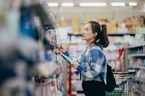Asian woman grocery shopping in supermarket and reading