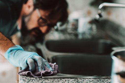 Close up view of man cleaning hard the kitchen surface at home in female usually work activity. Living alone male people using sponge and cleaner with perfection. Indoor work house concept. Husband