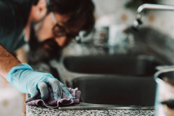 Close up view of man cleaning hard the kitchen surface at home in female usually work activity. Living alone male people using sponge and cleaner with perfection. Indoor work house concept. Husband stock photo