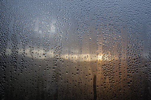 Condensation on window with a stormy sunrise outside, waterdrops on the glass.