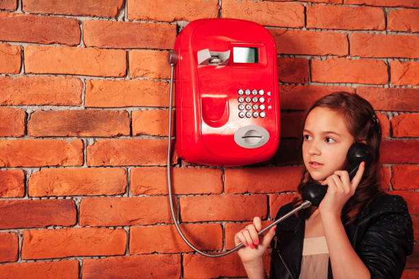 modèle d’adolescente en veste en cuir appelant vieux téléphone rouge de fond de mur de briques, regardant au loin. adolescente parlant téléphone à l’extérieur. concept de style de vie de communication. copier l’espace texte - pay phone brick wall telephone old photos et images de collection