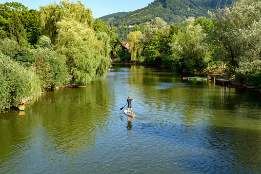 Man standing on sup board and paddling on beautiful green river Krka at Kostanjevica na Krki in Slovenia.