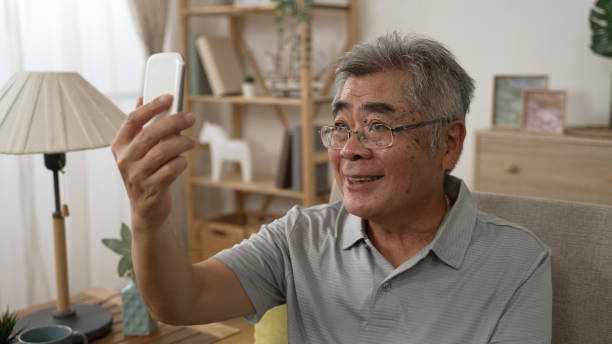 istock grandfather make video call to relatives with smartphone at home. Concept technology modern generation family connection. old asian Japanese man waving hand on couch and talking online by cellphone 1454328410