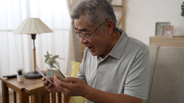 istock happy old man sit on sofa looking cellphone screen and raising hands. Modern wireless technology easy usage of older generation people concept. excited senior male winner check lottery paper on phone 1454329695