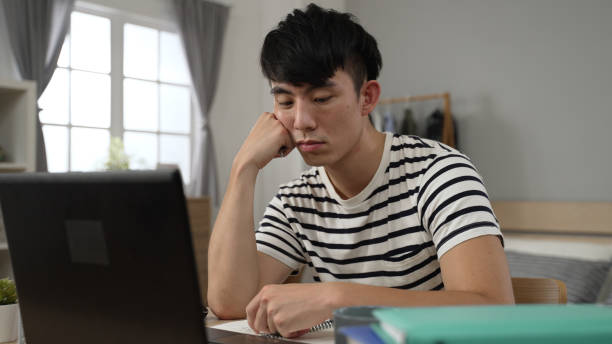 istock bored asian adult student learning from home is propping face and playing with pen while taking online courses on the computer in the bedroom during lockdown. 1454331301