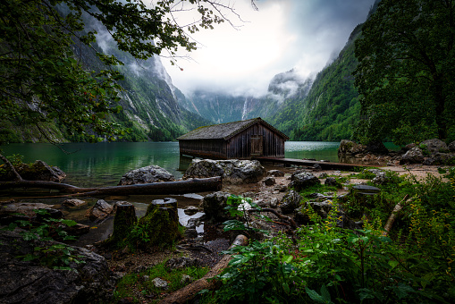 A scenic view of a wooden hut near the lake surrounded by mountains