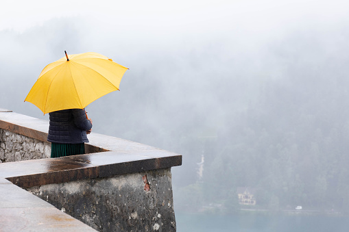 A lady with a yellow umbrella at a viewpoint on a rainy, foggy day