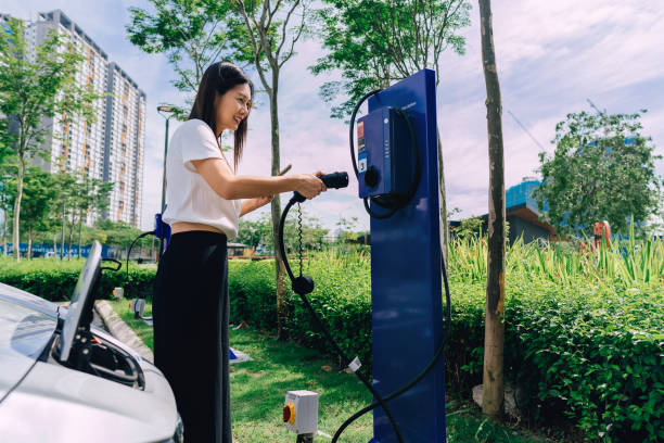 mujer en el estacionamiento, sosteniendo un enchufe de cargador de automóvil. - color image car futuristic road trip fotografías e imágenes de stock