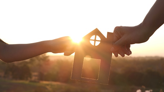 Mother and daughter hands holding paper house, home together silhouette against sunset with soft focus. Concept of Happy Family, Buy House, Home, life, insurance, care, saving, mortgage, estate