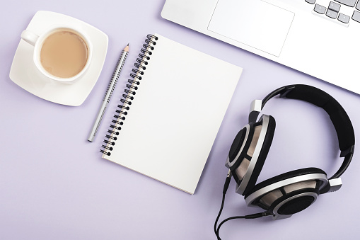 Notepad, coffee cup, laptop and headphones on lilac background. Top view, flat lay, mockup.