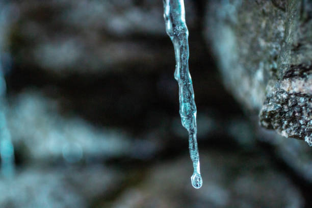 Icicles hang off eavestrough in sunlight and lofty clouds in sky