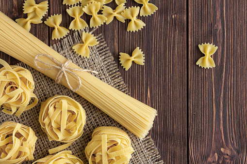 Different kinds of raw pasta with copy space on wooden background. Top view of Italian cuisine ingredient.