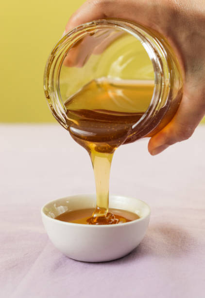 istock Hand pouring honey from a jar over a white bowl 1454343139