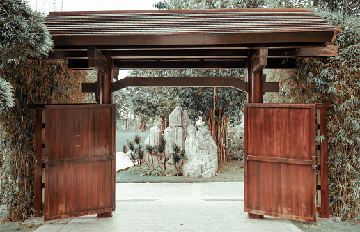 The wooden gates in Japanese style leading to beautiful park with dense vegetation and stone pieces
