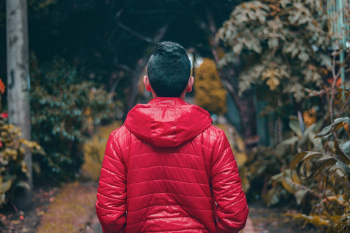 A young male wearing a red coat walking in a park